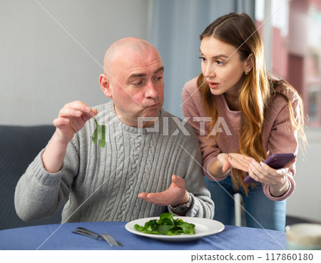 Wife with smartphone explaining health benefits of salad to her husband 117860180