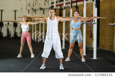 Man together with other athletes, does a warm-up using a long stick in gym Man together with other athletes, does a warm-up using a long stick in gym 117860318