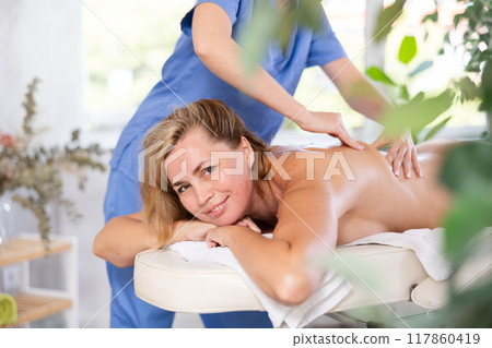 Portrait of woman enjoying relaxing massage by professional masseur Portrait of woman enjoying relaxing massage by professional masseur 117860419