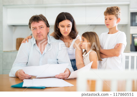Wistful father looking through papers with family Wistful father looking through papers with family 117860551