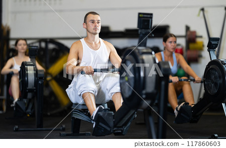 Young man exercising on rowing machine 117860603
