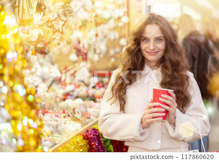 Happy woman walking through Christmas fair with cup of hot coffee 117860620