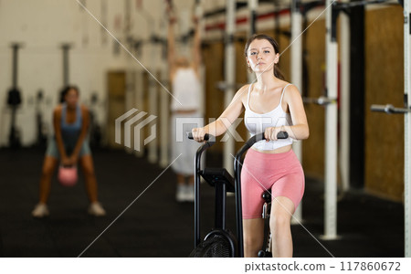 Portrait of young athletic girl training on an air-bike in gym 117860672