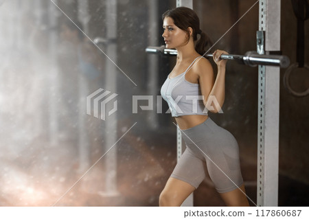 Young woman lifting barbell in gym 117860687