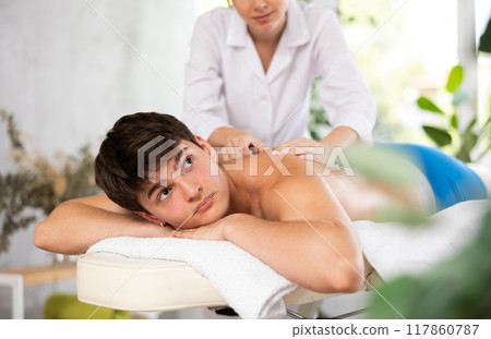 Relaxed young man having back massage therapy conducted by masseuse 117860787