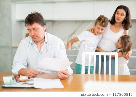 Worried adult man examining documents and counting money at table with family 117860815