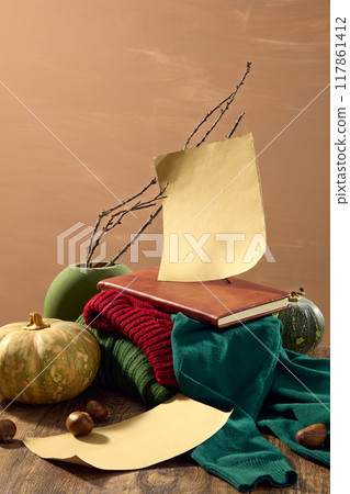 Autumn concept photo for advertising with some autumn items like pumpkin, chestnut, note book and colorful sweater placed on wooden table. Front angle shot on brown background Autumn concept photo for advertising with some autumn items like pumpkin, chestnut, note book and colorful sweater placed on wooden table. Front angle shot on brown background 117861412