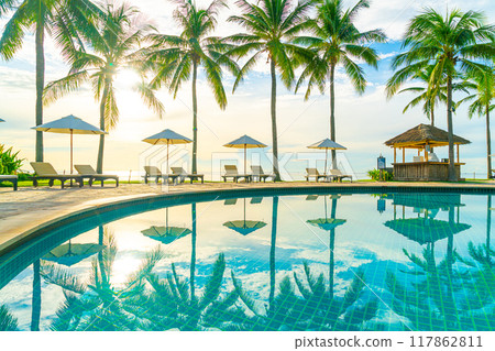Beautiful luxury umbrella and chair around outdoor swimming pool in hotel and resort with coconut palm tree on sunset or sunrise sky Beautiful luxury umbrella and chair around outdoor swimming pool in hotel and resort with coconut palm tree on sunset or sunrise sky 117862811
