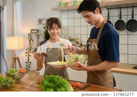 Cheerful couple preparing a fresh salad together in a modern kitchen. Healthy lifestyle concept Cheerful couple preparing a fresh salad together in a modern kitchen. Healthy lifestyle concept 117863277