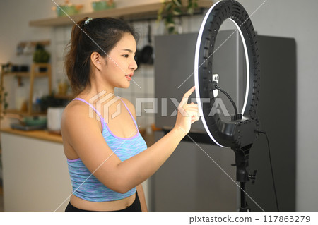 Young fitness woman fitness recording video online training with mobile phone camera in kitchen 117863279