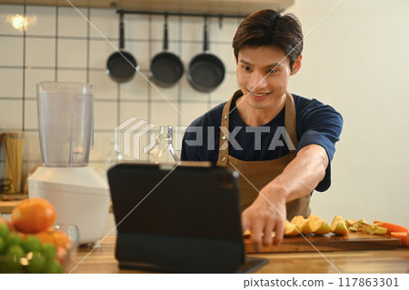 Handsome adult man making healthy smoothie and following online recipe on digital tablet Handsome adult man making healthy smoothie and following online recipe on digital tablet 117863301