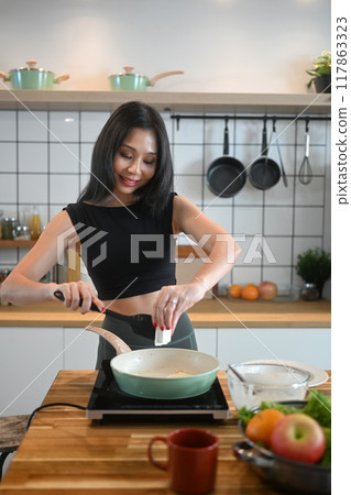 Happy young woman preparing a healthy meal in kitchen. Health lifestyle and wellness concept 117863323