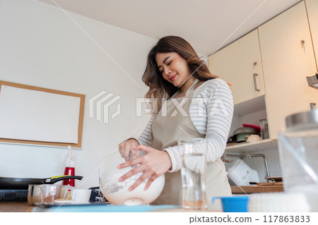 Smiling baker woman creating homemade delights in home kitchen Smiling baker woman creating homemade delights in home kitchen 117863833