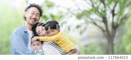 Banner of a family playing in a park with fresh green leaves, looking at the camera 117864023