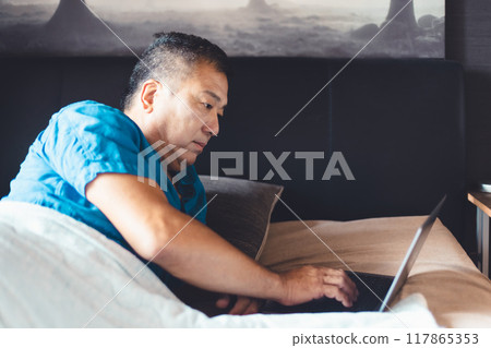Man using a laptop in bed 117865353