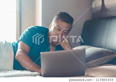 Man using a laptop in bed 117865354