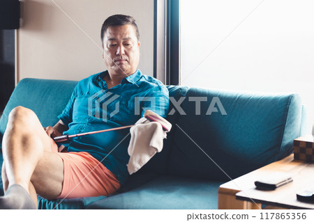 一個男人在客廳照顧高爾夫球桿 117865356