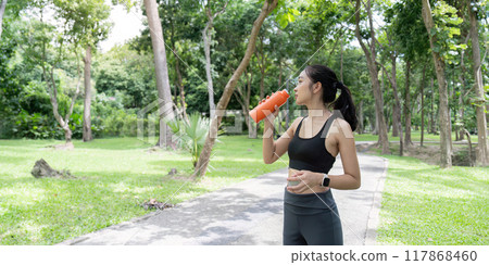 Asian woman hydrating with bottle amidst park workout routine 117868460