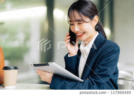 一位女士在咖啡館的露臺上拿著平板電腦打電話 117868489