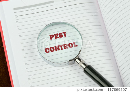 Pest control phrase written through a magnifying glass on a blank page of a notebook, a book 117869307