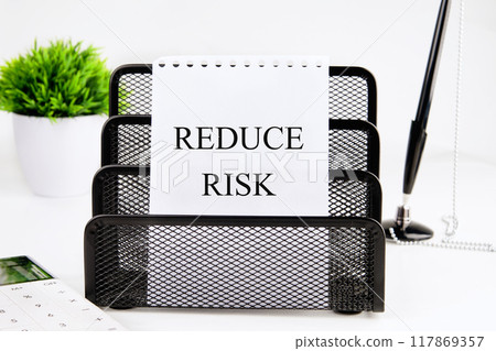 Conceptual reduce risk symbol. Copy space. Words REDUCE RISK on a white sheet of paper in a stationery stand on a white background 117869357
