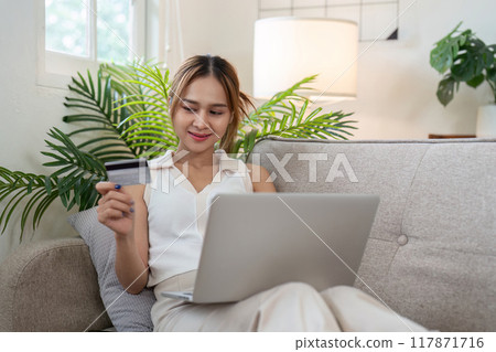 Cheerful Asian woman using credit card for online shopping at home Cheerful Asian woman using credit card for online shopping at home 117871716