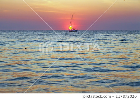 Picture of a sailing yacht on the sea in front of the setting sun in back light 117872020