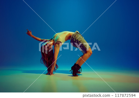 Flexible, talented, artistic young woman dancing high heels dance, performing against blue studio background in neon light 117872594