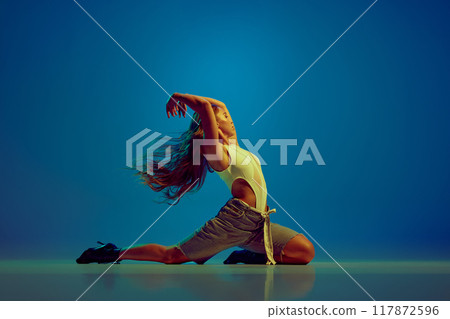 Passionate and sensual woman, young elegant dancer performing high heels dance against blue studio background in neon light 117872596