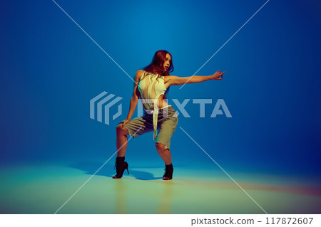 Sensual young beautiful woman dancing high heel dance, performing against blue studio background in neon light Sensual young beautiful woman dancing high heel dance, performing against blue studio background in neon light 117872607