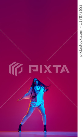 Vertical image of young woman in oversized t-shirt and heeled shoes dancing against magenta studio background Vertical image of young woman in oversized t-shirt and heeled shoes dancing against magenta studio background 117872652