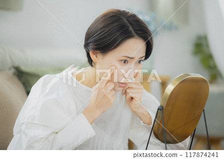 Middle-aged woman looking in the mirror in the living room 117874241