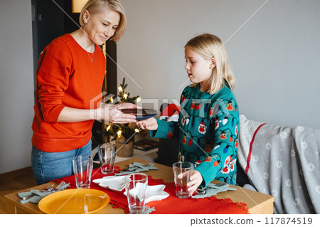 Mother and daughter setting the table for Christmas dinner, holiday meal preparation, festive family traditions, Christmas Eve, quality time, togetherness. Mother and daughter setting the table for Christmas dinner, holiday meal preparation, festive family traditions, Christmas Eve, quality time, togetherness. 117874519