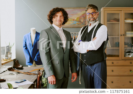 Mature tailor and young brutal model in gray suit smiling while posing for phone in atelier 117875161