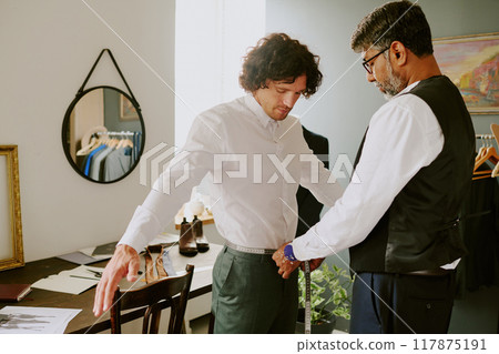 Highly skilled Indian tailor taking hip measurements of male customer in atelier 117875191