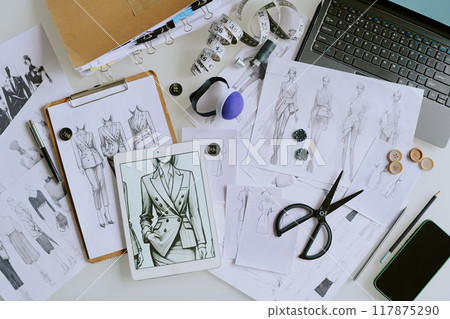 Top down shot of white table with sketches of new collection female clothes and digital device Top down shot of white table with sketches of new collection female clothes and digital device 117875290