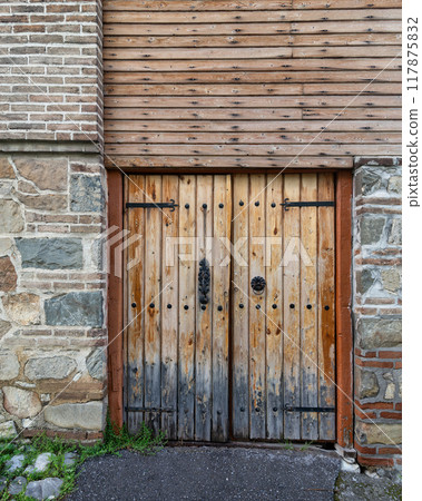 Historic Wooden Door With Detailed Ironwork and Stone Wall, Located in a Rustic Village Setting During Daylight 117875832