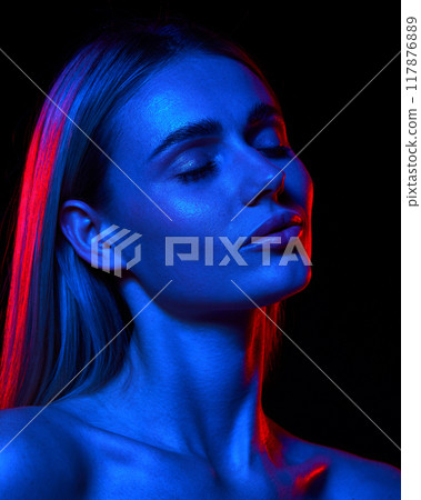 Beautiful young woman with pristine, clear skin illustrating results of skincare against black studio background in neon light Beautiful young woman with pristine, clear skin illustrating results of skincare against black studio background in neon light 117876889