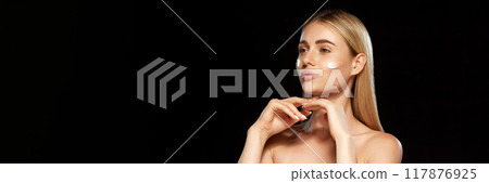 Portrait of beautiful young woman with well-kept healthy skin, applying face cream against black studio background Portrait of beautiful young woman with well-kept healthy skin, applying face cream against black studio background 117876925