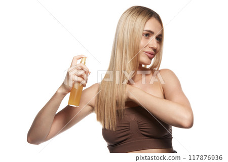 Beautiful woman with flawless blonde hair demonstrates the impact of high-quality hair care and cosmetic treatments, using hair spray 117876936