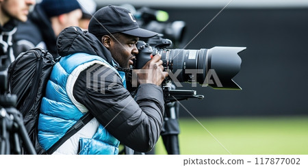 Focused and engaged sports photographer in action, capturing moments with large telephoto lens camera. 117877002