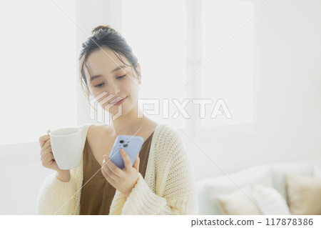 一位年輕女子在房間裡看著她的智慧型手機 117878386