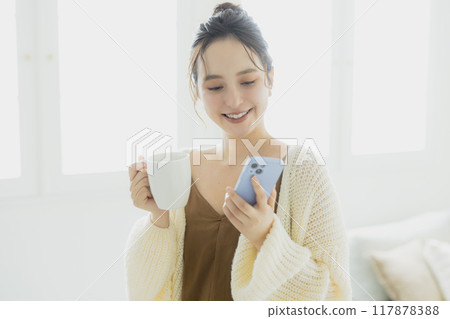 Young woman looking at her smartphone in her room 117878388