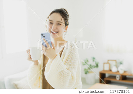 Young woman looking at her smartphone in her room Young woman looking at her smartphone in her room 117878391