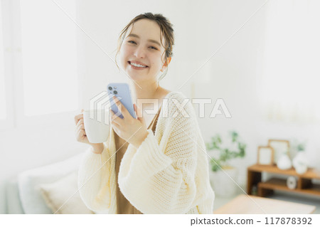 一位年輕女子在房間裡看著她的智慧型手機 一位年輕女子在房間裡看著她的智慧型手機 117878392