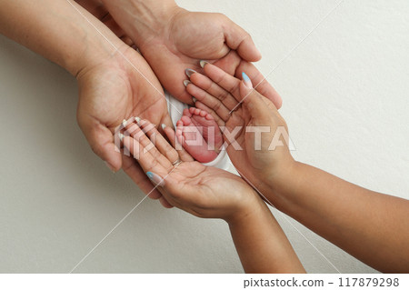 The palms of the parents. A father and mother hold the feet of a newborn child in a white blanket on a white background.. The feet of a newborn in the hands of parents. Photo of foot, heels and toes The palms of the parents. A father and mother hold the feet of a newborn child in a white blanket on a white background.. The feet of a newborn in the hands of parents. Photo of foot, heels and toes 117879298