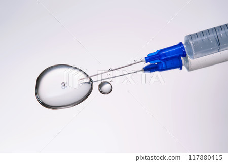 A drop of medicine flowing from a syringe with a needle. 117880415