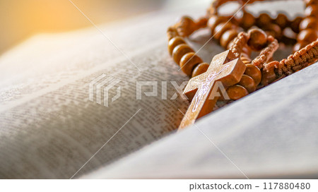 Dark brown wooden cross on an old open book symbolizing the spread of Jesus Christs love among Christians reflecting faith devotion and the importance of Christian teachings. 117880480