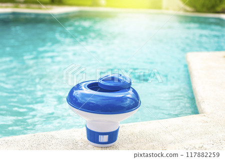 A chlorine dispenser for swimming pools with blue water in the background. Dosing float for swimming pool chlorination, A chlorine float on the edge of a swimming pool. A chlorine dispenser for swimming pools with blue water in the background. Dosing float for swimming pool chlorination, A chlorine float on the edge of a swimming pool. 117882259