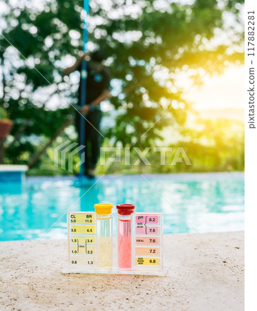 Water PH tester kit on the edge of the swimming pool with maintenance person in the background 117882281